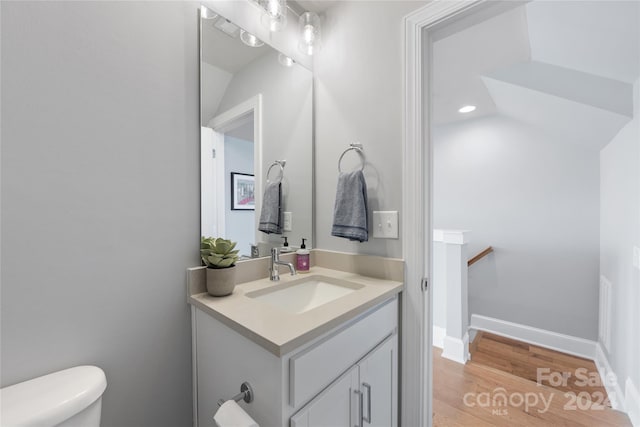 bathroom featuring vanity, toilet, wood-type flooring, and vaulted ceiling