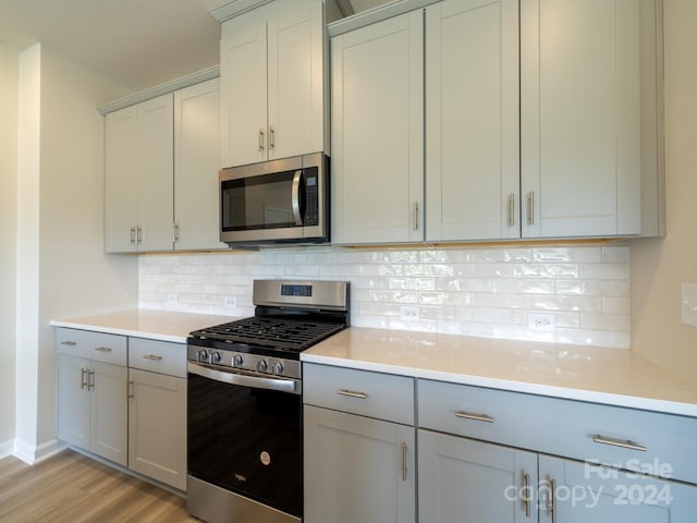 kitchen with gas range oven, light hardwood / wood-style flooring, gray cabinets, and backsplash