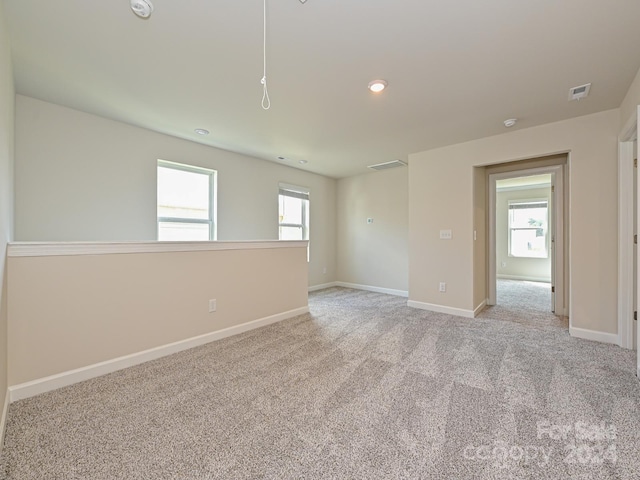 empty room with a wealth of natural light, light colored carpet, visible vents, and baseboards