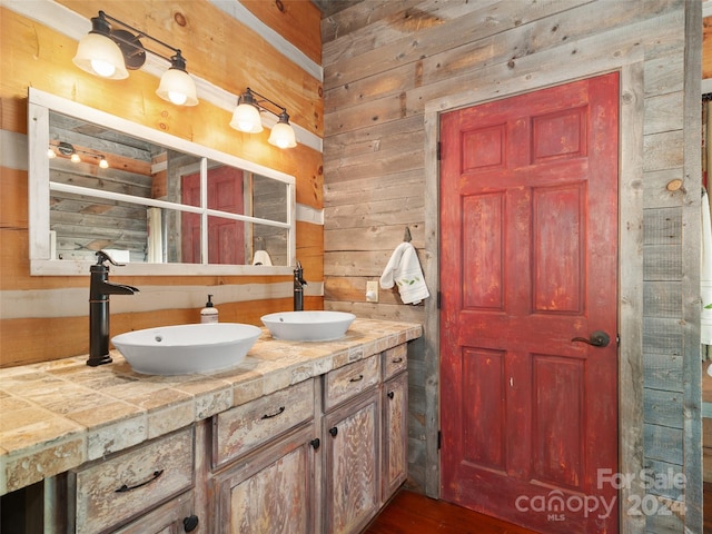 bathroom with dual vanity, wooden walls, and hardwood / wood-style floors