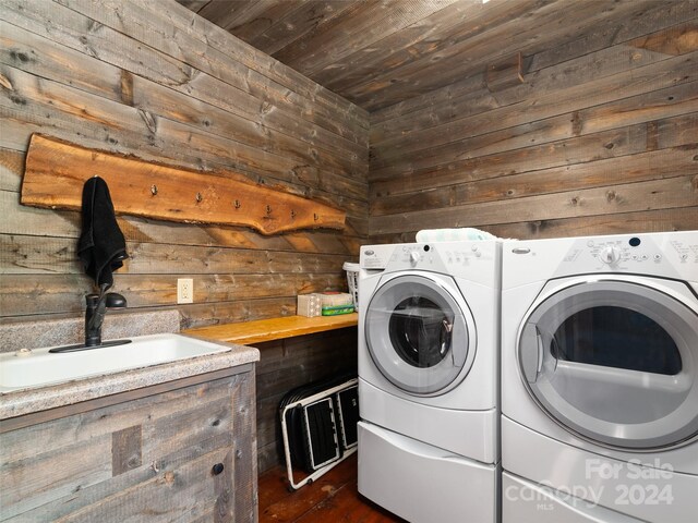 laundry room with dark wood-type flooring, wood walls, washer and dryer, wood ceiling, and sink