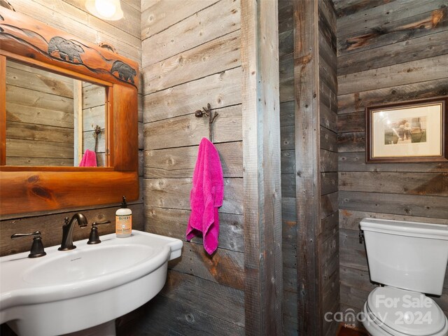 bathroom with sink, wooden walls, and toilet