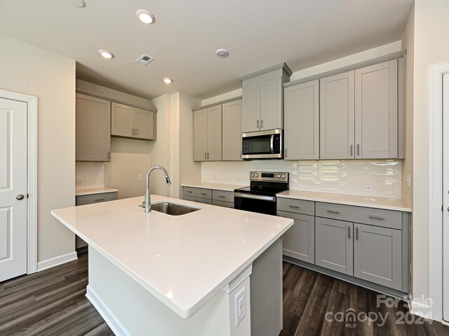 kitchen featuring dark wood-type flooring, stainless steel appliances, a center island with sink, sink, and tasteful backsplash