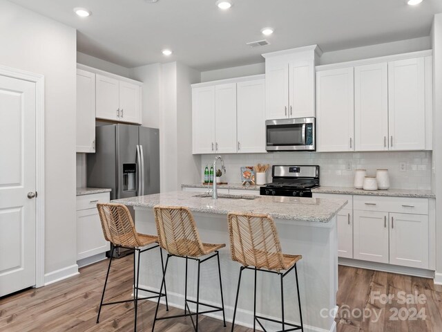 kitchen with tasteful backsplash, appliances with stainless steel finishes, an island with sink, light hardwood / wood-style floors, and sink