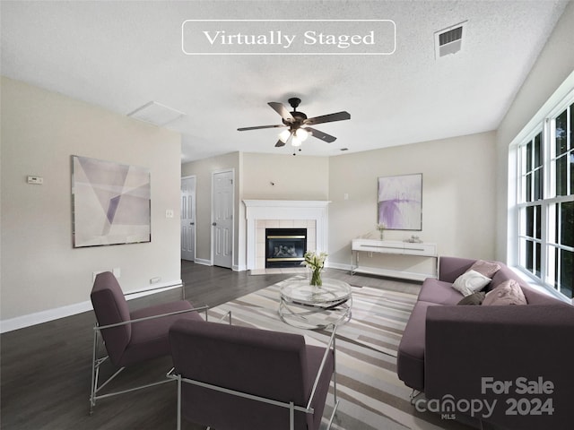 living room with dark hardwood / wood-style floors, ceiling fan, a textured ceiling, and a tile fireplace