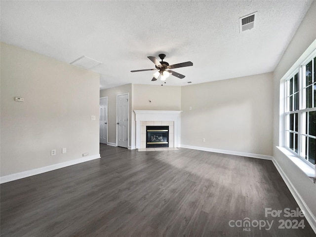 unfurnished living room with a textured ceiling, ceiling fan, dark wood-type flooring, and a tiled fireplace