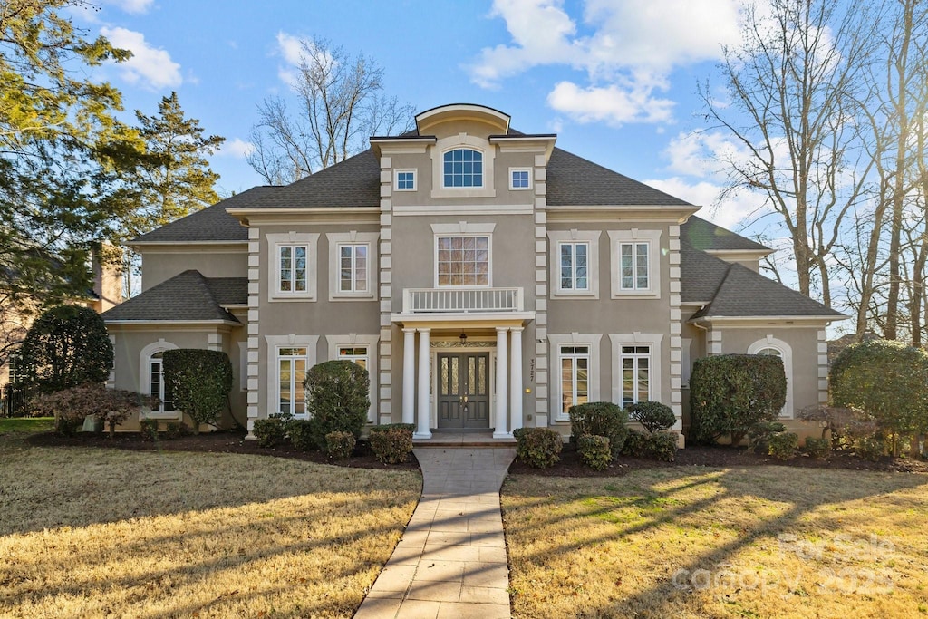 colonial house with a shingled roof, a front lawn, french doors, and stucco siding