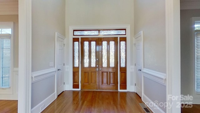 entrance foyer with a high ceiling, visible vents, wood finished floors, and wainscoting