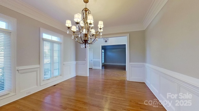 unfurnished dining area with a wainscoted wall, ornamental molding, a chandelier, and wood finished floors