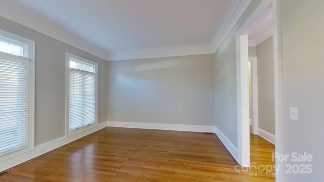 spare room featuring baseboards, wood finished floors, visible vents, and crown molding