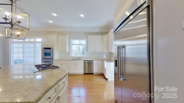 kitchen with appliances with stainless steel finishes, light stone countertops, light wood-style floors, white cabinetry, and pendant lighting