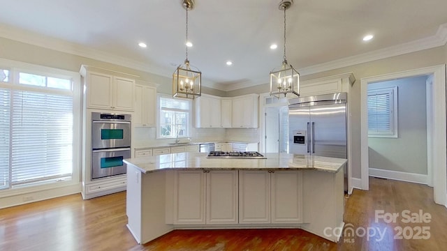 kitchen with stainless steel appliances, a sink, a kitchen island, light stone countertops, and decorative light fixtures