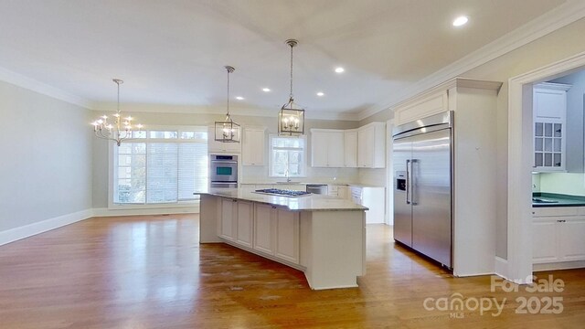 kitchen featuring white cabinets, a kitchen island, ornamental molding, decorative light fixtures, and stainless steel appliances