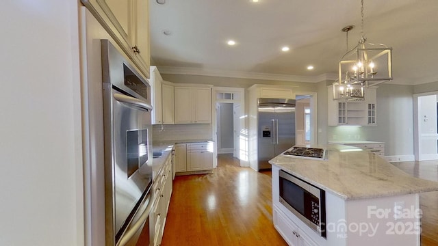 kitchen featuring light wood finished floors, a kitchen island, light stone counters, built in appliances, and hanging light fixtures