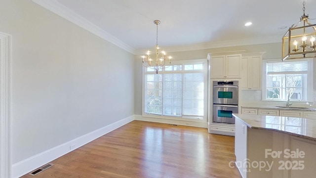 kitchen with hanging light fixtures, double oven, a sink, light stone countertops, and a chandelier