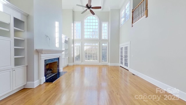 unfurnished living room featuring light wood-type flooring, a fireplace, baseboards, and ceiling fan