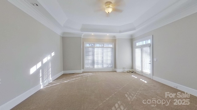 empty room with ornamental molding, a tray ceiling, and baseboards