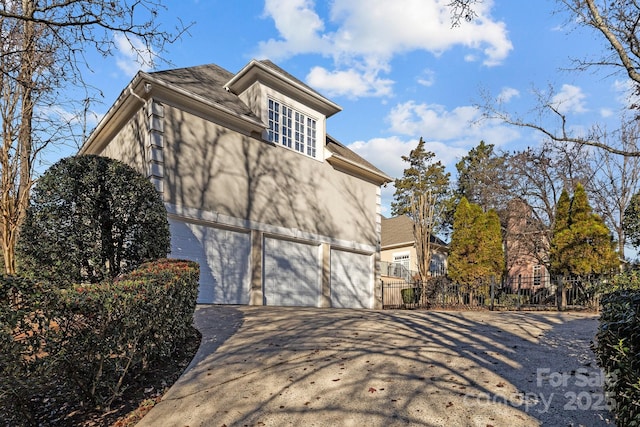 view of property exterior with a garage, concrete driveway, fence, and stucco siding