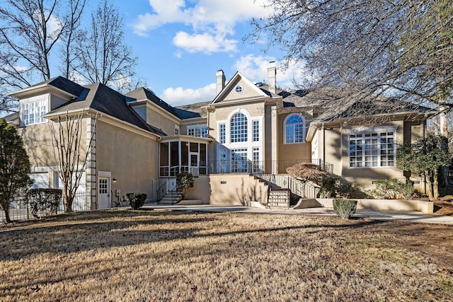 rear view of house with a sunroom, a yard, stairway, and stucco siding