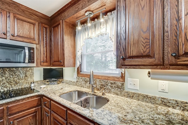 kitchen with hanging light fixtures, sink, black electric stovetop, and light stone countertops