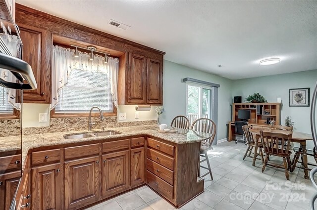 kitchen featuring light tile patterned floors, a kitchen bar, sink, and kitchen peninsula