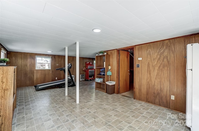 basement with wood walls, white refrigerator, and light tile patterned floors