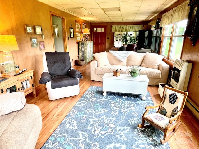 living room with heating unit, a paneled ceiling, hardwood / wood-style floors, and wooden walls