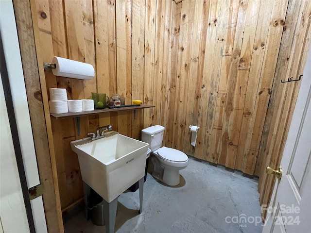 bathroom with concrete flooring, toilet, and wooden walls