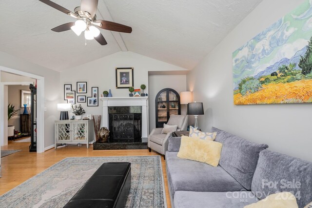 living room with a textured ceiling, a tile fireplace, light hardwood / wood-style flooring, and vaulted ceiling with beams