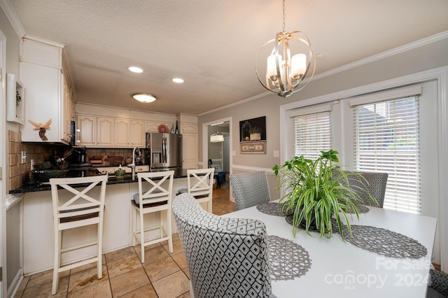 tiled dining room featuring sink, a textured ceiling, ornamental molding, and a chandelier