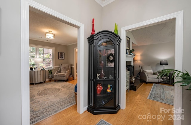 hallway with ornamental molding, wood-type flooring, and a textured ceiling