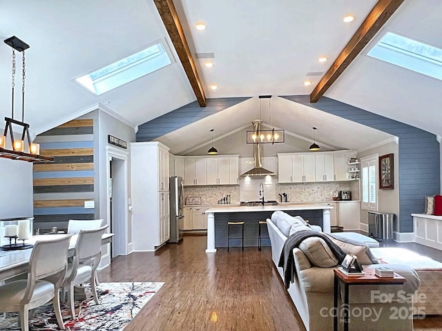 kitchen featuring sink, pendant lighting, white cabinetry, vaulted ceiling with skylight, and an island with sink