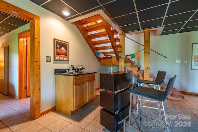 bar with light tile patterned floors and light brown cabinets