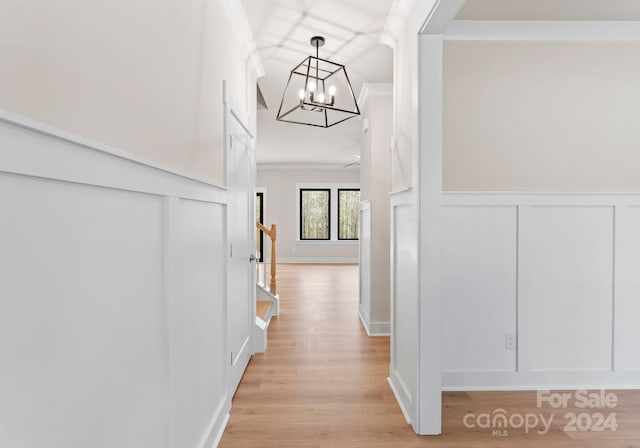 corridor featuring ornamental molding, an inviting chandelier, and light hardwood / wood-style flooring