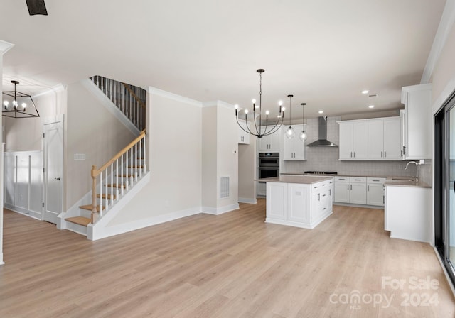 kitchen with pendant lighting, wall chimney exhaust hood, white cabinets, a kitchen island, and a chandelier