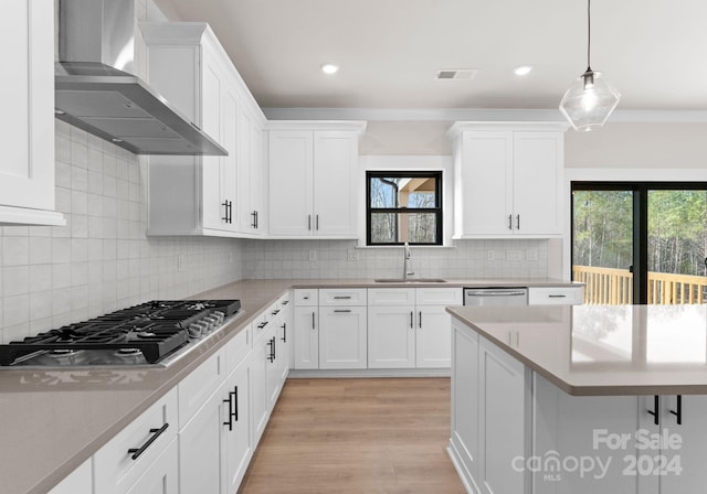 kitchen featuring white cabinets, decorative light fixtures, stainless steel appliances, and wall chimney exhaust hood