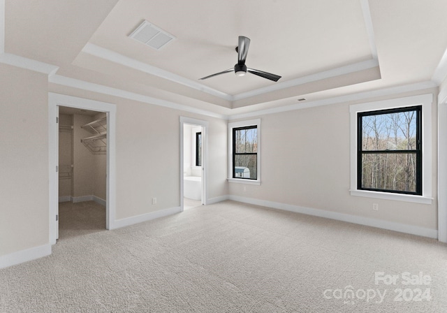 unfurnished bedroom featuring crown molding, a spacious closet, carpet floors, and a tray ceiling