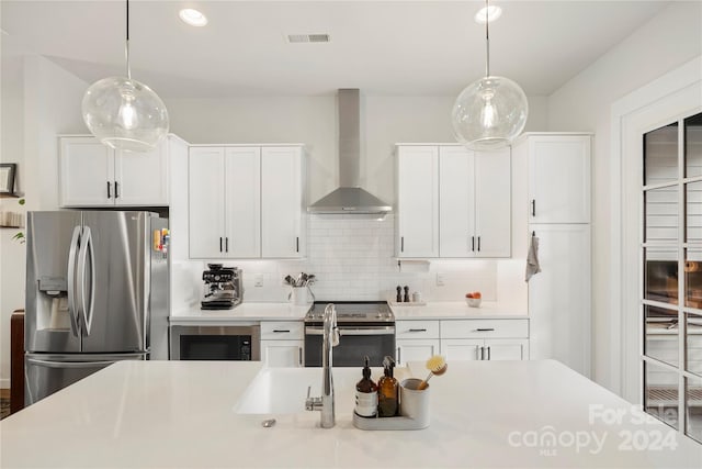 kitchen featuring appliances with stainless steel finishes, decorative backsplash, pendant lighting, wall chimney range hood, and white cabinets