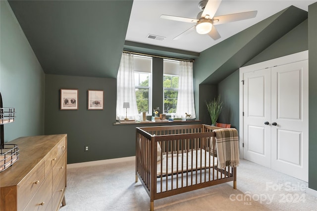 bedroom with a crib, a closet, vaulted ceiling, ceiling fan, and light colored carpet