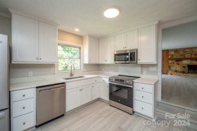 kitchen with white cabinets, ornamental molding, stainless steel appliances, and sink