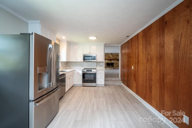 kitchen featuring stainless steel appliances, white cabinets, wood walls, and crown molding