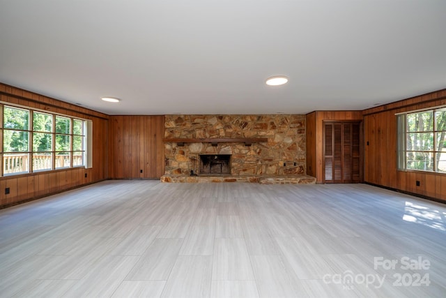 unfurnished living room featuring a stone fireplace and wood walls