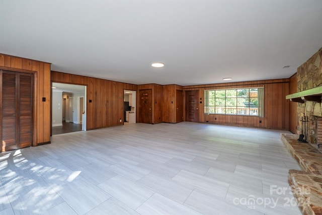 unfurnished living room featuring a stone fireplace and wood walls