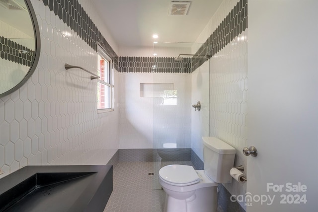 bathroom featuring a tile shower, tile walls, tile patterned flooring, and toilet