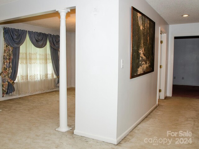 hall with decorative columns, a textured ceiling, and light colored carpet