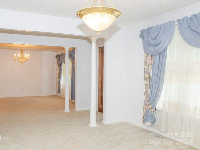 carpeted spare room with decorative columns, a notable chandelier, and a textured ceiling