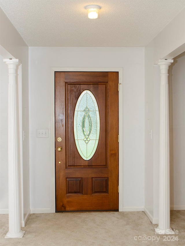 carpeted foyer featuring a textured ceiling and ornate columns