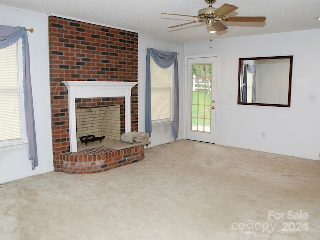 unfurnished living room featuring ceiling fan, a textured ceiling, carpet floors, and a brick fireplace