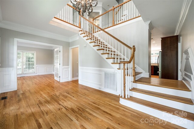 staircase featuring light wood-type flooring, ornamental molding, and a chandelier