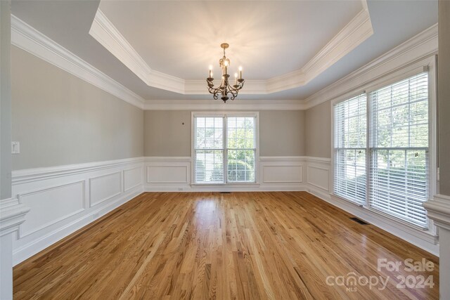 spare room featuring light wood-type flooring, crown molding, a chandelier, and a tray ceiling